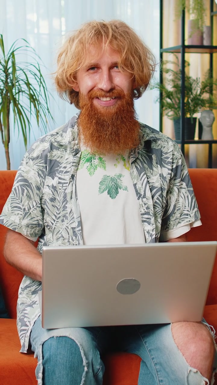 Rødhåret mandlig freelancer begynder at arbejde på sin bærbare computer, sender beskeder og foretager onlinekøb hjemmefra.