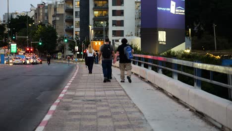 people walking down the bridge on pedestrian sidewalk by a busy road, tel aviv israel