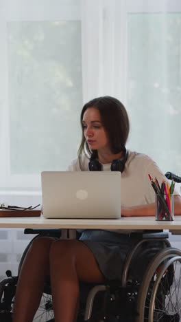mujer con discapacidad en silla de ruedas habla con su amiga mientras hace tareas en la computadora portátil. estudiantes inteligentes discuten la vida universitaria completando la tarea en la habitación