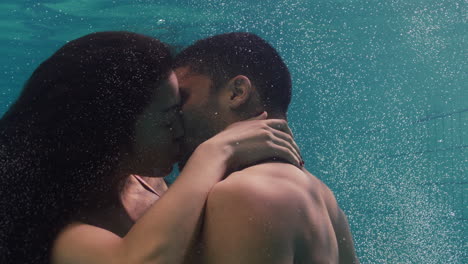 young couple kissing underwater in swimming pool enjoying intimate kiss romantic lovers submerged in water floating with bubbles in passionate intimacy