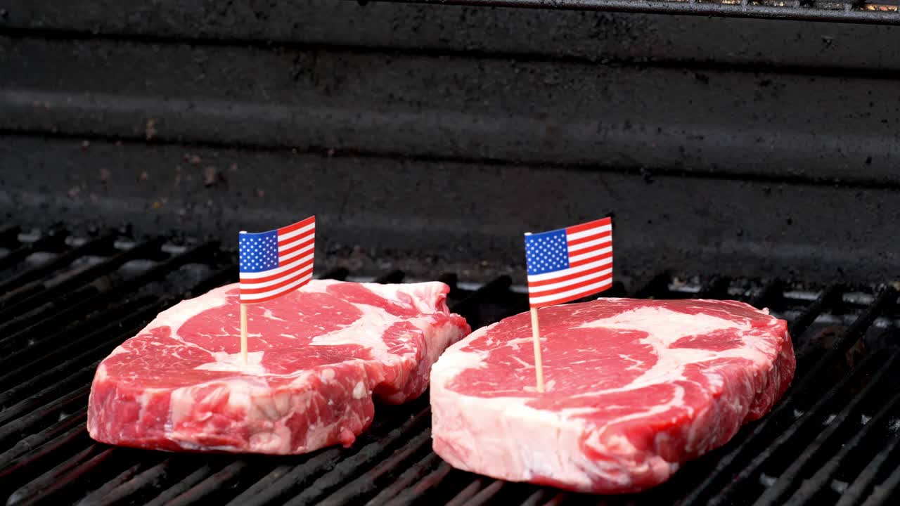 그릴에 앉아 두 개의 작은 미국 국기 이빨로 요리하는 두 개의 육즙이 많은 립아이 스테이크