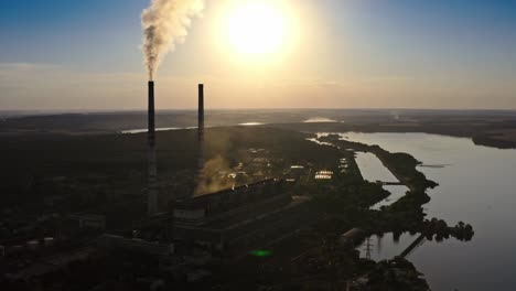 fábrica oscura contra el sol poniente naranja. tuberías de la fábrica con humo. humo sucio se derrama de las chimeneas en el aire en el fondo del río. video de vista aérea.