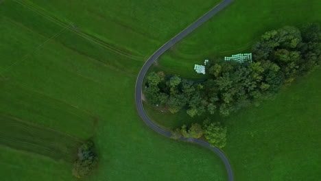 Asphalt-road-bending-in-green-countryside-field-with-stored-hay-bales