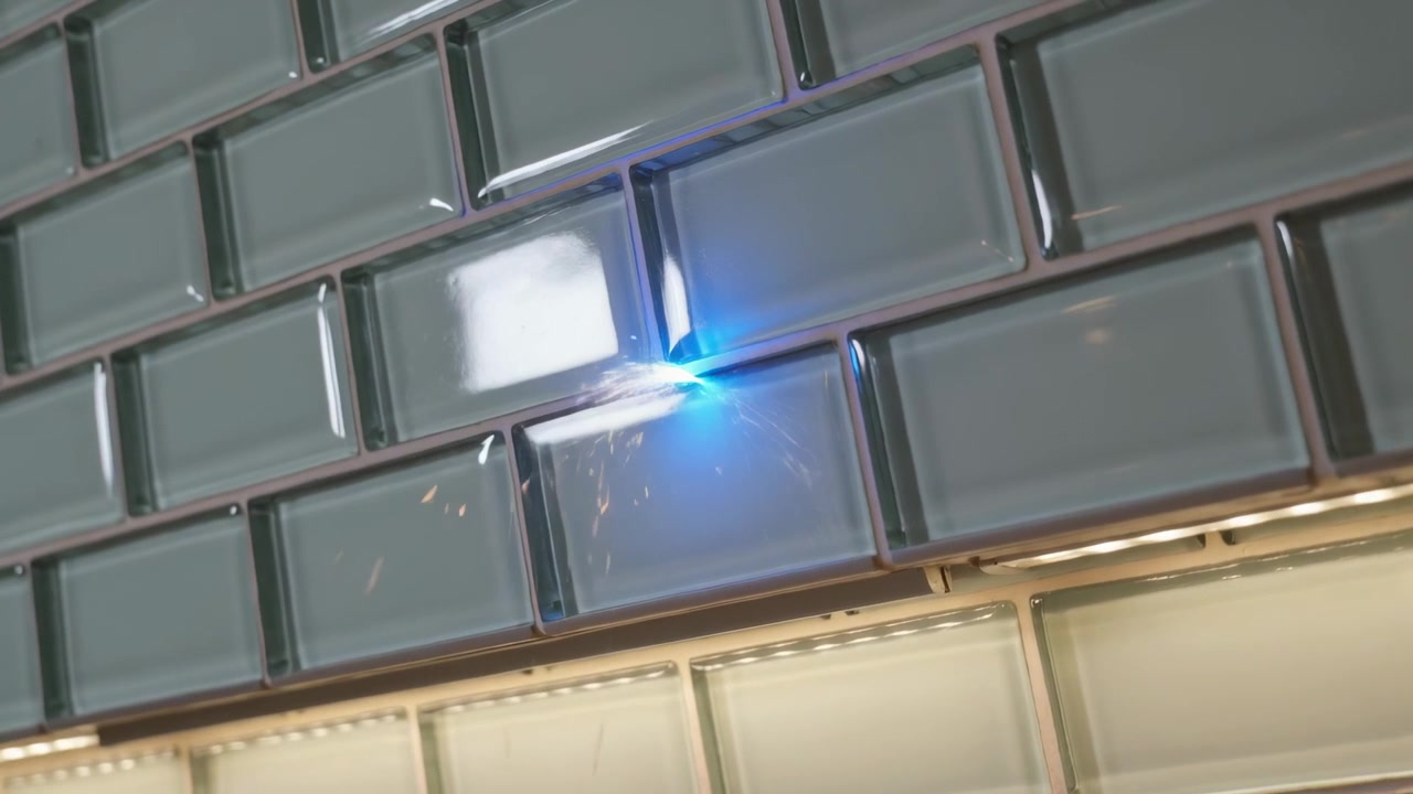 Un punto blu emergente pulsa sulla fuga delle piastrelle lucide tipo metropolitana, emettendo scintille con riflessi.
