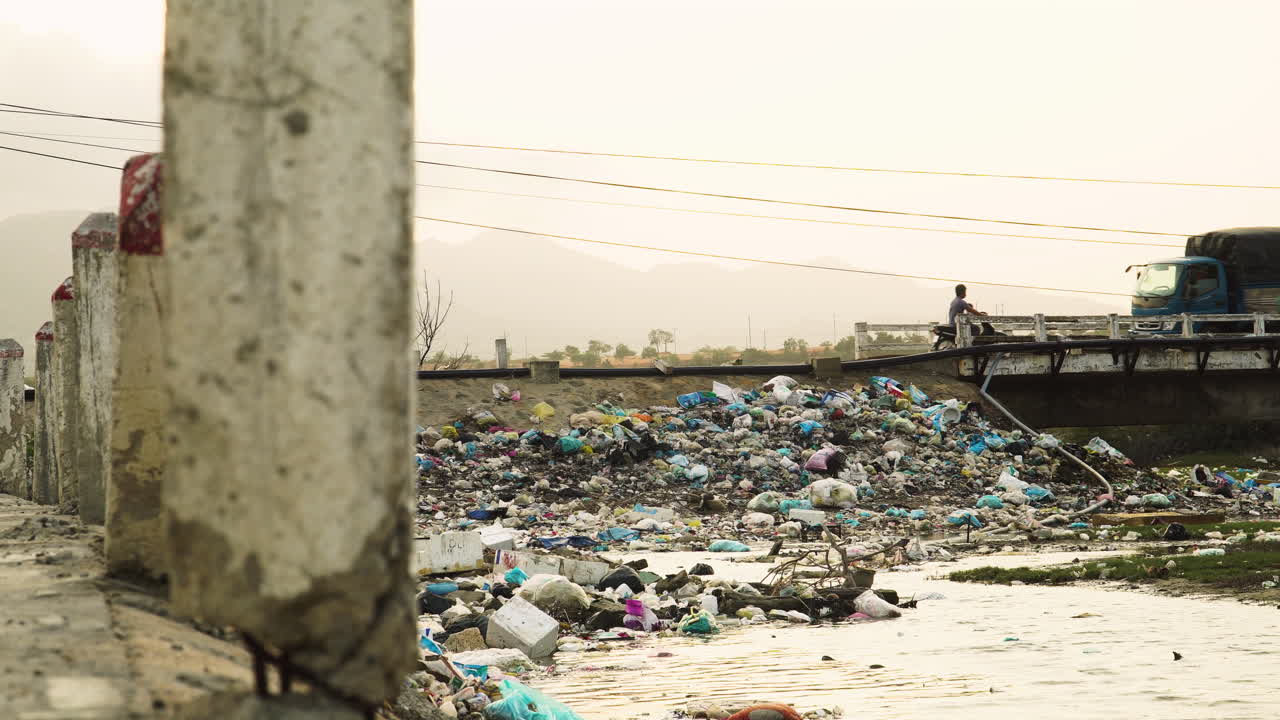 Traffic over city bridge in Vietnam, garbage accumulated on river bank