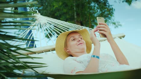 portrait of a woman on vacation. lies in a hammock, uses a smartphone