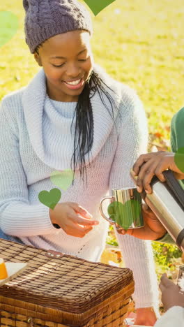 animation of green hearts over picnic basket and african american family in park