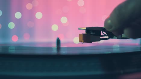 the moment of a rotating vinyl plate turntable on a pink background and bright bokeh lights. sound technology for dj to mix and play music. the man's hand puts and removes needle from the vinyl plate