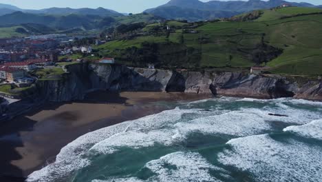 cantabrian sea waves break onto sand beach below tall angled rock cliff