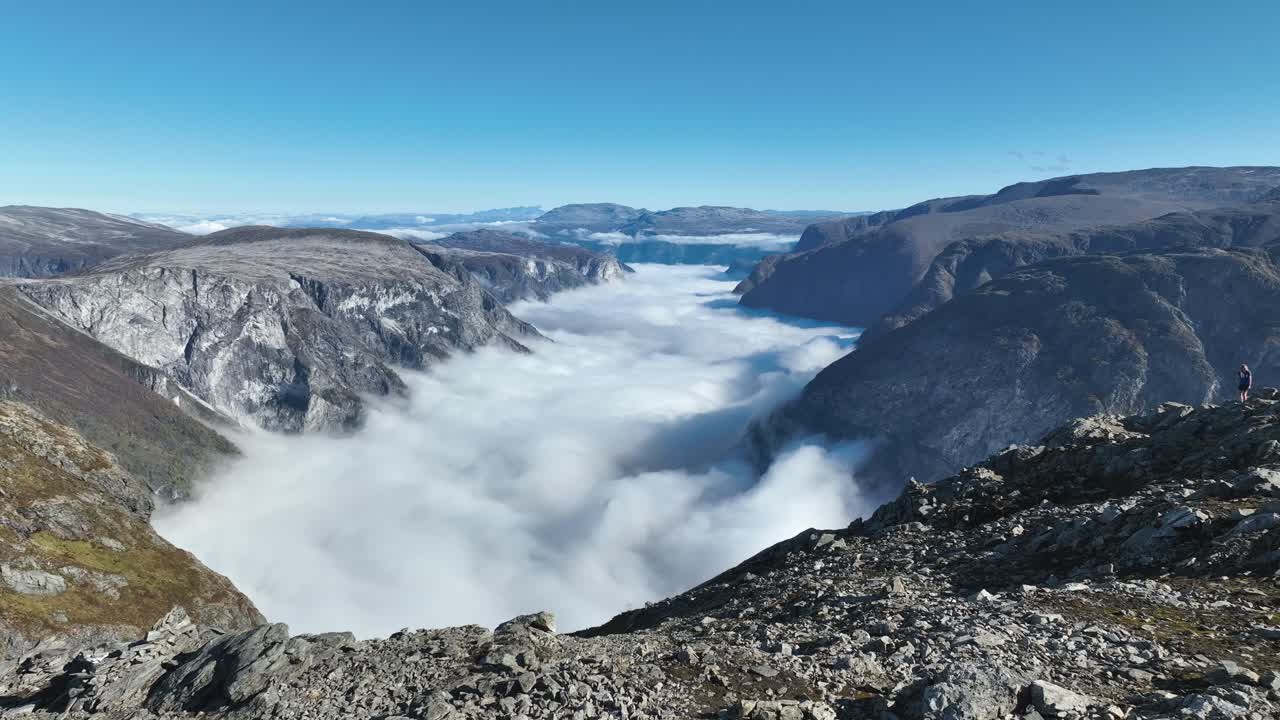 Drone flies sideways close to Bakkanosi rocky top, creating a parallax effect with Naeroyfjord and Breiskrednosi in the distance