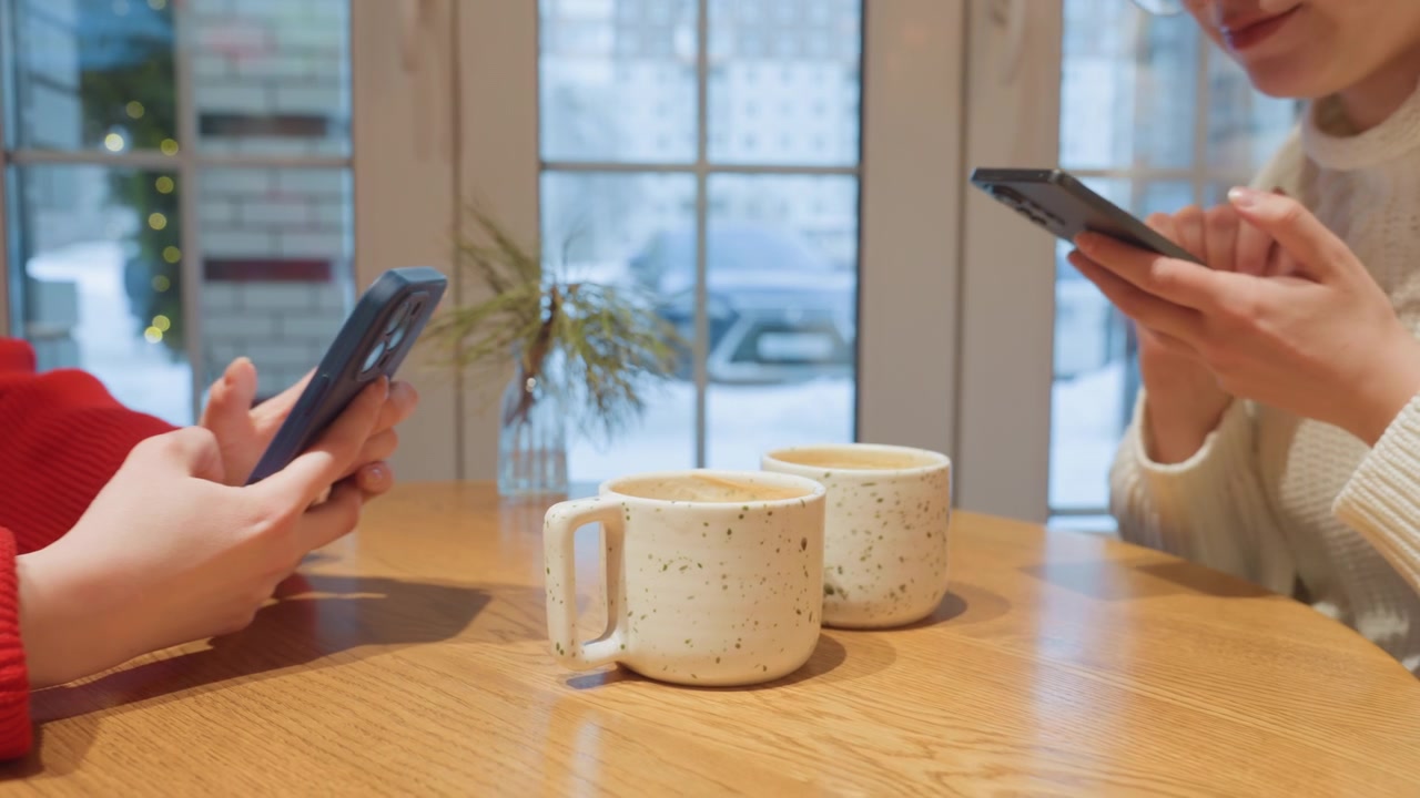 カフェでスマートフォンを使いながらコーヒーを飲む二人