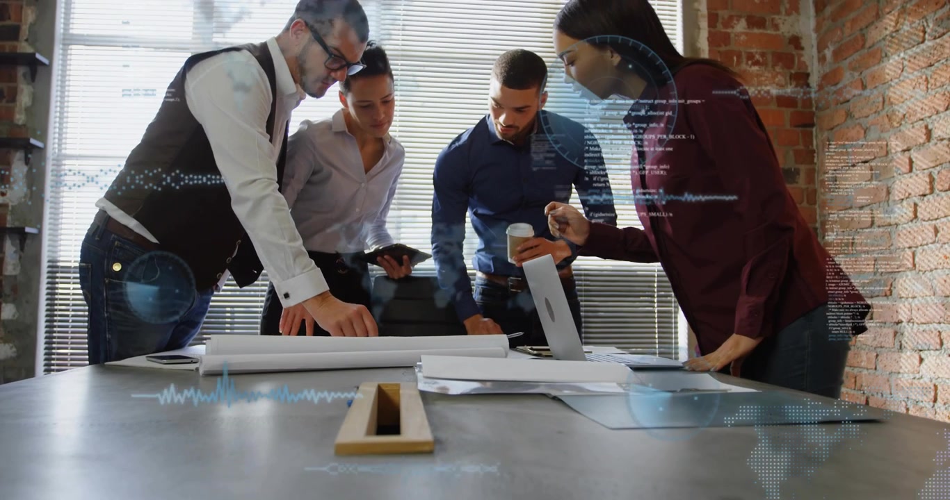 Design team pointing pen over plans, consulting laptop starting overlays showing graphs for review