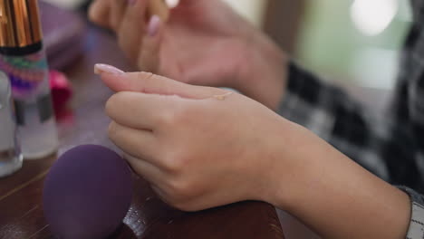 closeup partial view of lady dispensing liquid powder onto hand before blending with beauty sponge. smooth application technique highlights skincare routine and flawless makeup