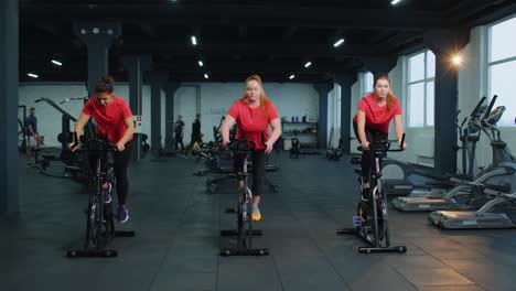 grupo de mujeres atléticas en bicicleta estacionaria rutina de entrenamiento en gimnasio, pérdida de peso en interiores