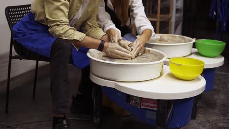 cheerful, smilling couple having fun while working together in potter workshop. sitting by potter's wheel, marking each other noses with clay. slow motion