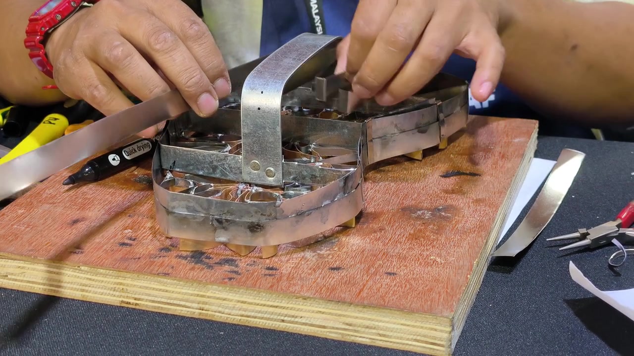 A craftsman creates a copper batik stamp. This traditional Malay art tool is dipped in hot wax to stamp patterns onto fabric. It saves time compared to hand-drawing.