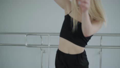 fit girl in black clothes performing contemporary. female dancer shows flowing motions, body and hands waves at white room. modern ballet dance choreography. young woman is moving smoothly