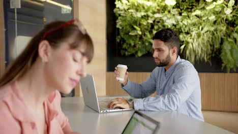 working in office, man using laptop and holding coffee cup, woman using tablet