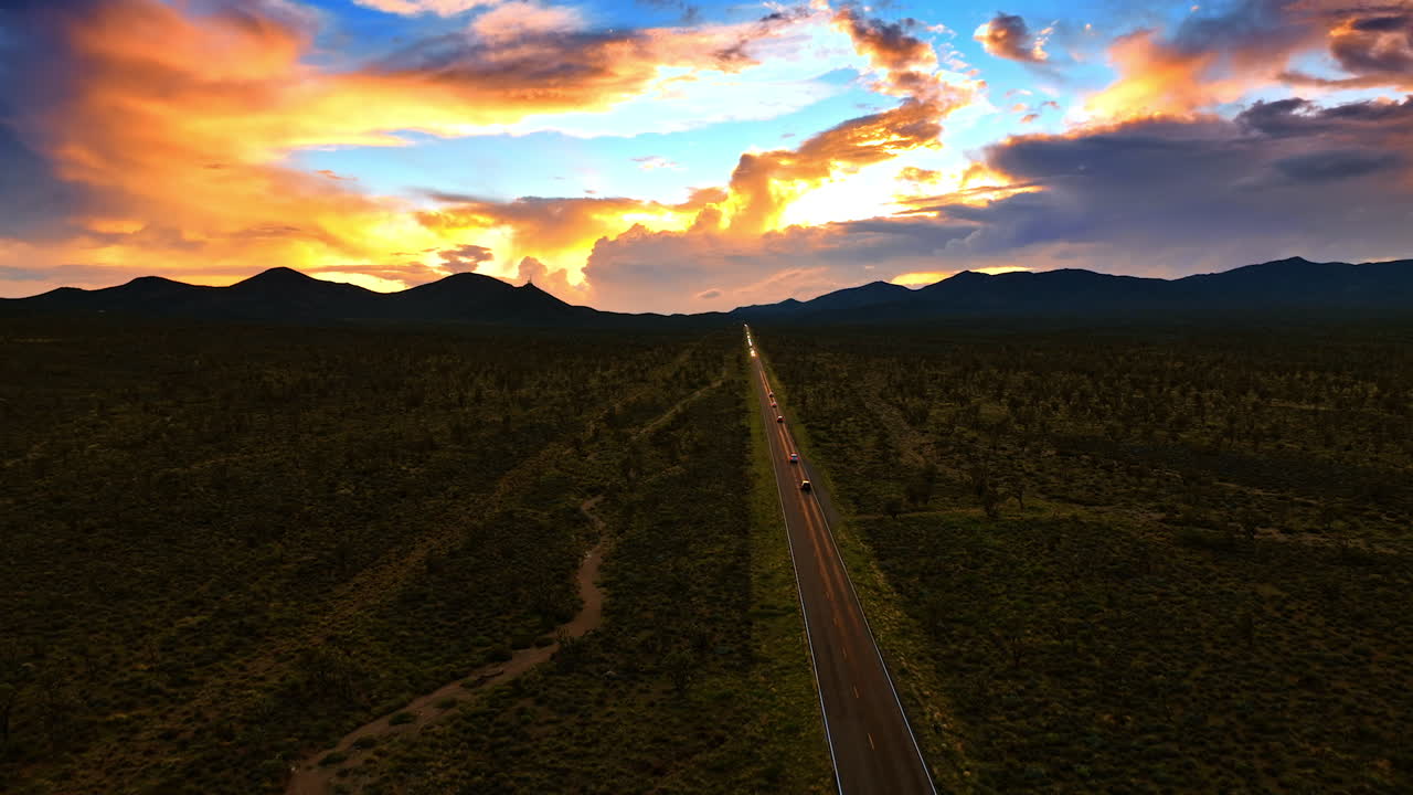 Cars ride by the straight highway through the Death Valley in California. Colorful clouds are in the sky at backdrop.