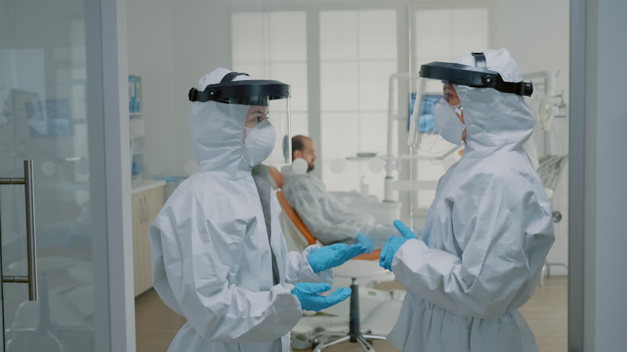 바이러스 보호복을 입은 치과의사들이 치과 절차에 대해 이야기하고 있습니다.