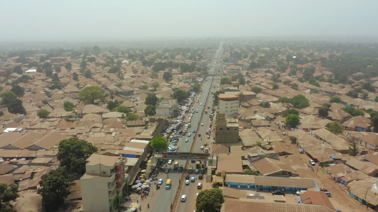 Drone shot capturing the densely populated capital city of Bissau, Guinea-Bissau, West Africa. Showcasing the unique urban sprawl, brown rooftops, central traffic, and surrounding green landscape