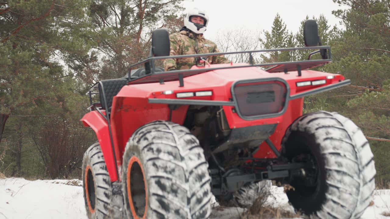 Primo piano del frontale di un ATV con pilota in bianco, pneumatici con battistrada robusto e cerchi arancioni che sollevano spruzzi di neve, trazione delle ruote su sentiero ghiacciato, movimento della sospensione visibile, prestazioni fuoristrada intense, focus tecnico.