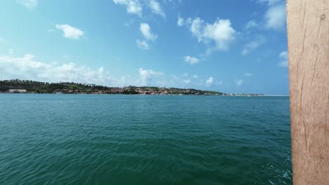 Tilt-up-slow-motion-action-camera-shot-from-aboard-a-small-guide-boat-on-a-tropical-crystal-clear-turquoise-river-near-the-beach-town-of-Barra-do-Cunhaú-in-Rio-Grande-do-Norte,-Brazil-on-a-summer-day