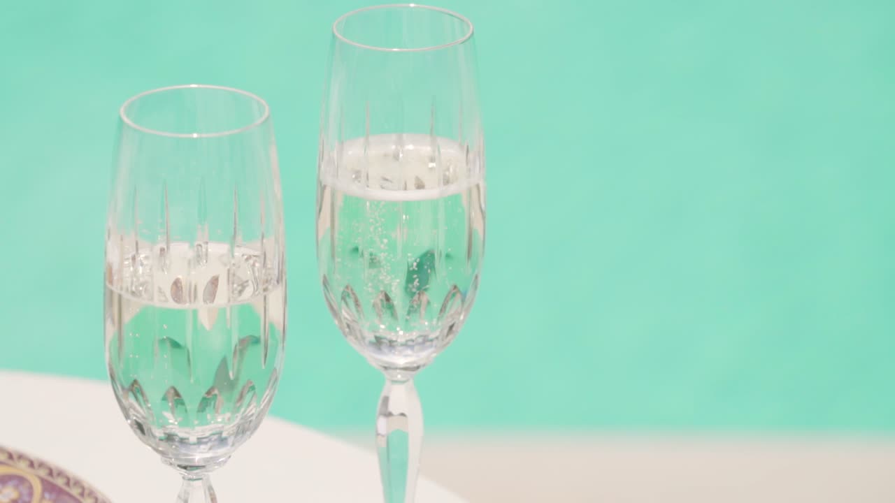 dos vasos de champán de vino blanco en una mesa con agua clara de la piscina en el fondo