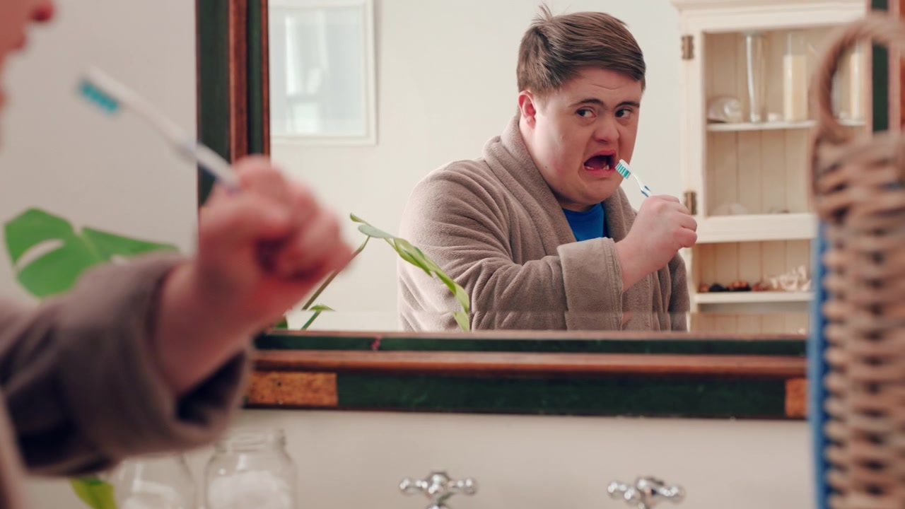 Young Man with Down Syndrome Brushing Teeth in Bathroom Mirror