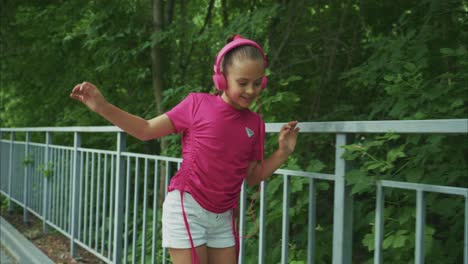 a young girl in pink headphones enjoys the outdoors while listening to music, showcasing confidence and joy as she moves gracefully along a path surrounded by lush greenery