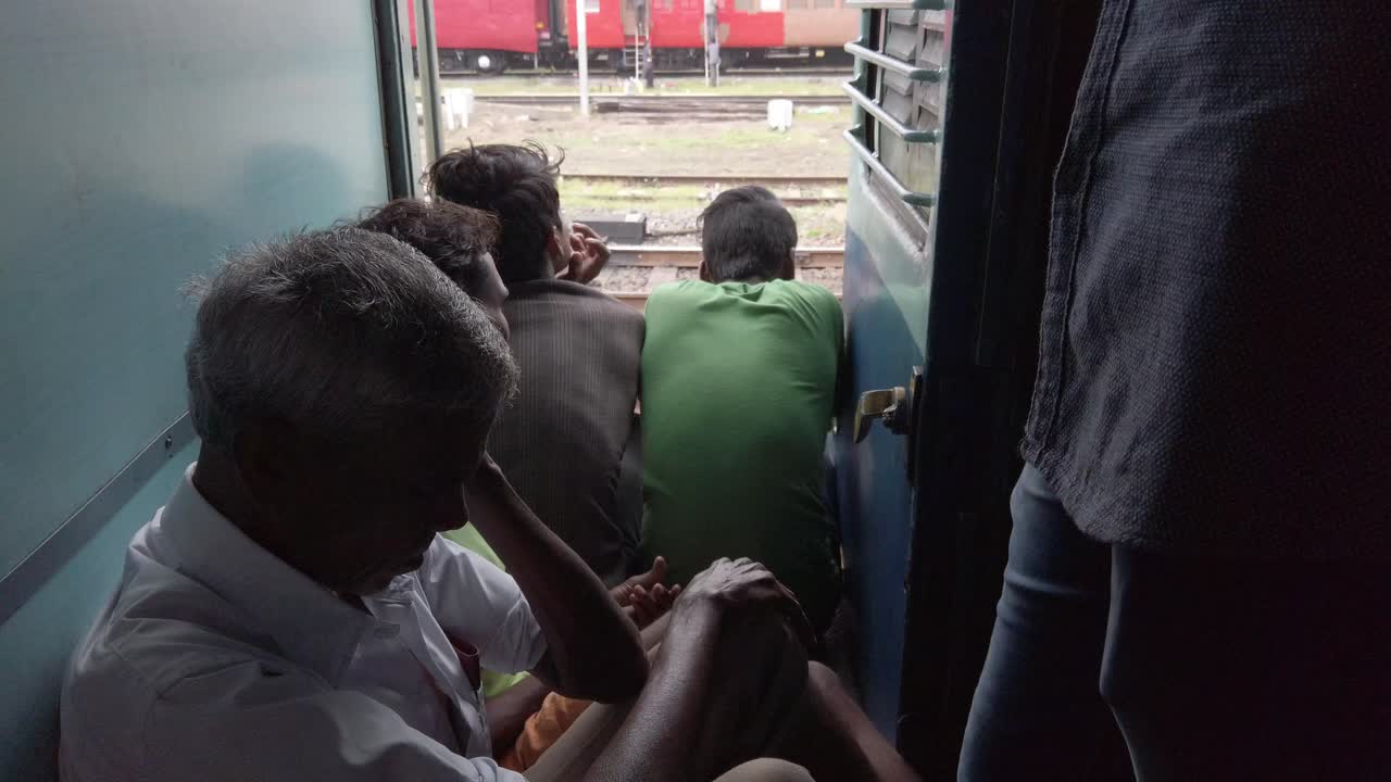 Passengers sitting near the exit door of a train compartment in a crowded train