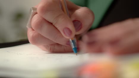 Primer-Plano-De-La-Mano-De-Una-Mujer-Escribiendo-Con-Un-Bolígrafo-En-Una-Hoja-De-Papel