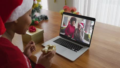 Mujer-Afroamericana-Con-Sombrero-De-Santa-Usando-Una-Computadora-Portátil-Para-Una-Videollamada-Navideña-Con-La-Familia-En-La-Pantalla