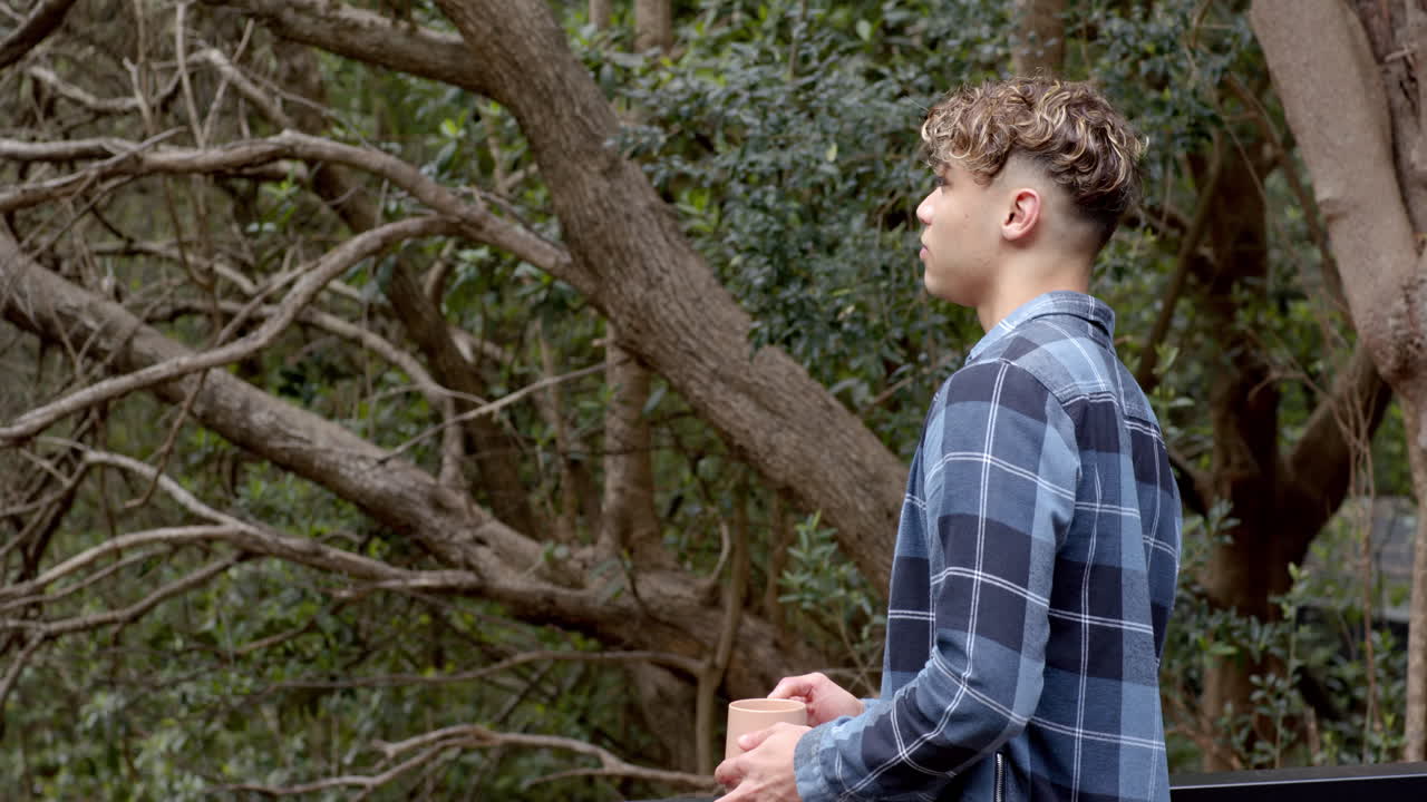 Young man holding coffee cup, enjoying peaceful moment in forest