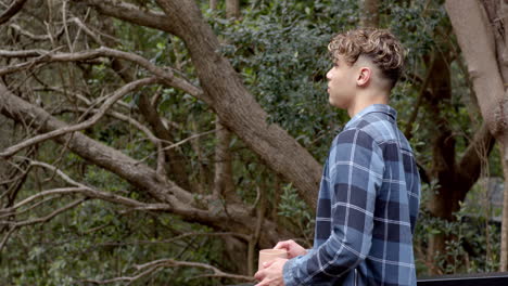 young man holding coffee cup, enjoying peaceful moment in forest