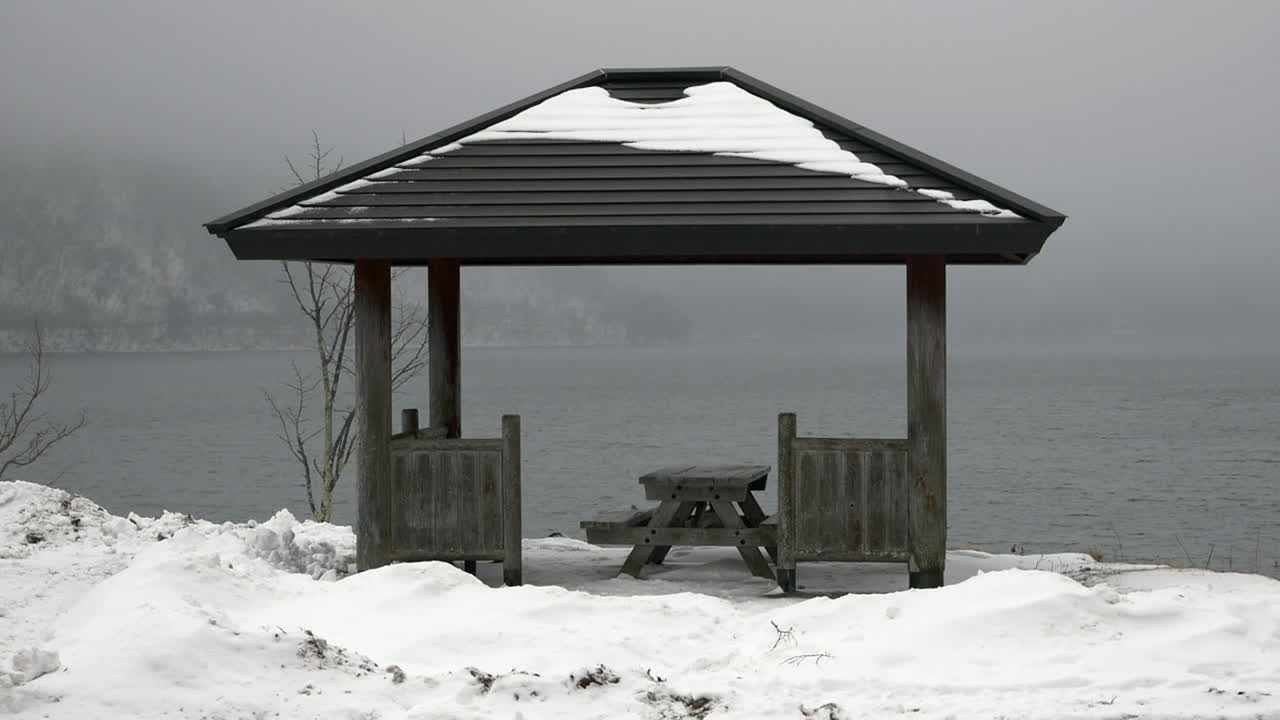 Traffic driving by a lonely snow covered roadside picnic gazebo alongside Lake Chuzenji, Japan