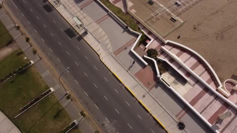 Toma-Aérea-De-Arriba-Hacia-Abajo-De-Un-Hombre-Corriendo-En-Una-Pasarela-Al-Lado-De-Una-Playa-Exótica-Durante-Un-Día-Soleado-En-Verano---Ciudad-De-Mar-Del-Plata,-Argentina