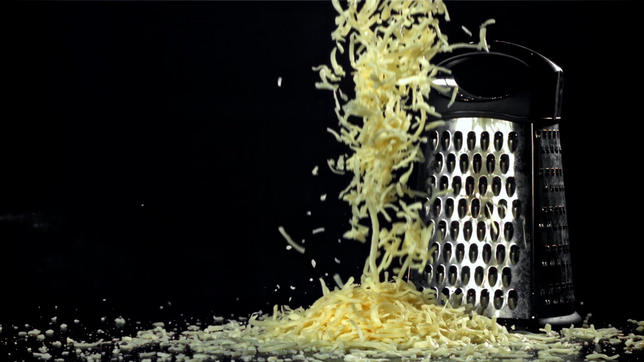 Formaggio grattugiato che cade al rallentatore con una grattugia su sfondo nero