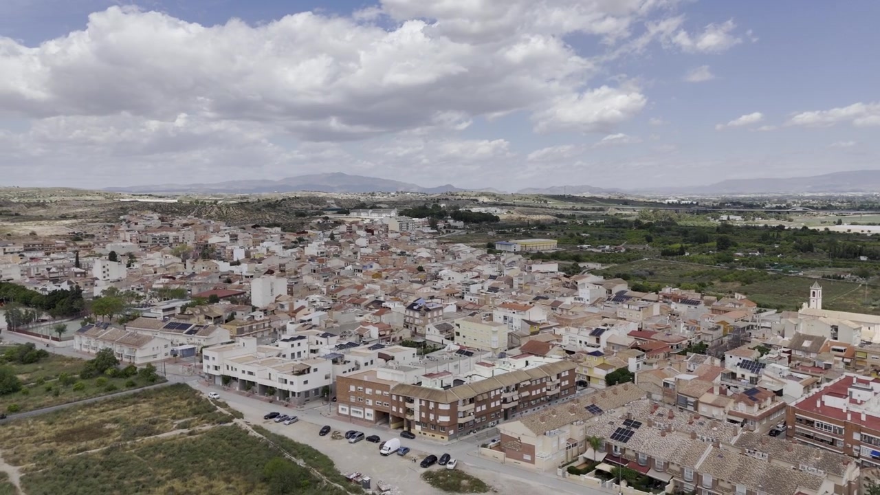 Riprese aeree panoramiche sui tetti di Javali, campi coltivati circostanti e strade rurali sotto un cielo nuvoloso e luminoso