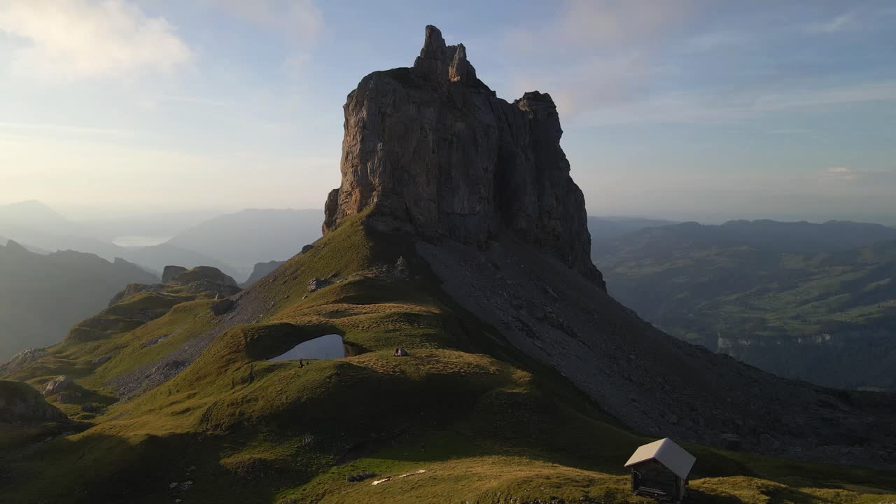 Drone slow pull in footage showcasing the Gross Achslenstock, Schwyz, Switzerland bathed in the warm glow of sunrise, its rugged beauty and the serene swiss alps landscape surrounding it