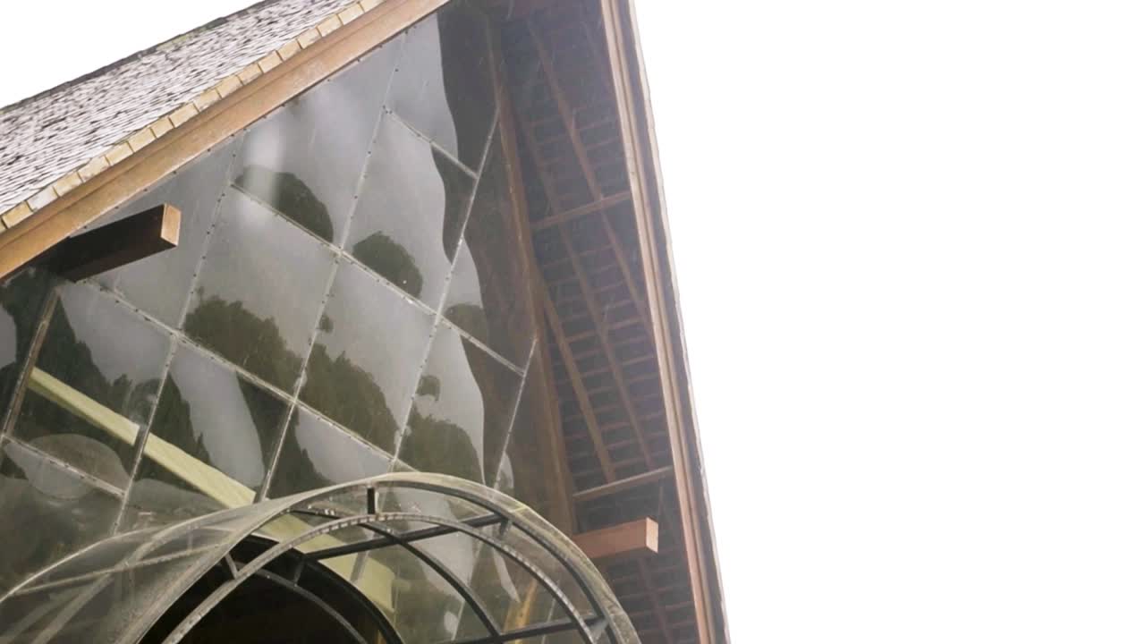 el agua gotea de las hojas de palma que cubren una choza tropical para revelar un edificio de vidrio.