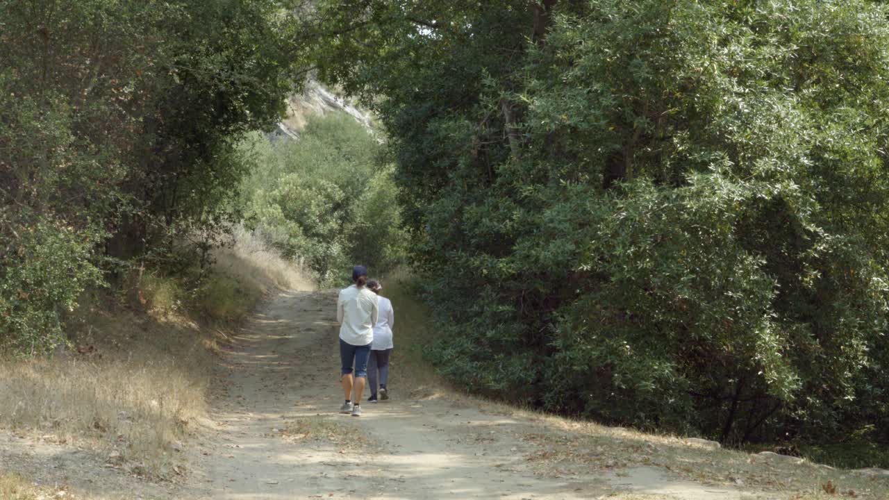 una maestra del instituto braille ayuda a una estudiante ciega a usar su bastón blanco para caminar por un camino de tierra en el bosque de california