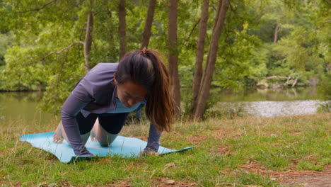 woman wearing sports clothing doing yoga on mat in forest by lake or river enjoying peace and beauty of nature