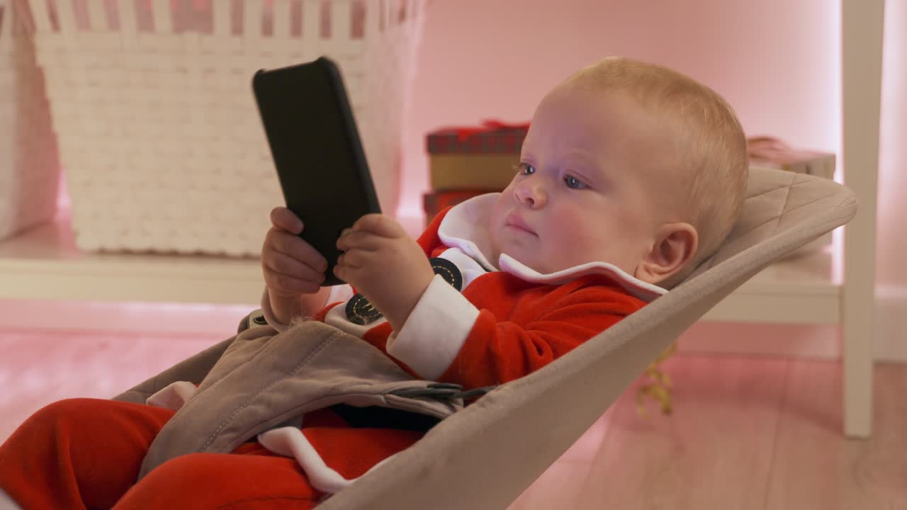 サンタクロースの服を着た子供が携帯電話で遊んで楽しんでいます スマートフォンの画面を見ている幸せな子供が 最初の新年を祝っています