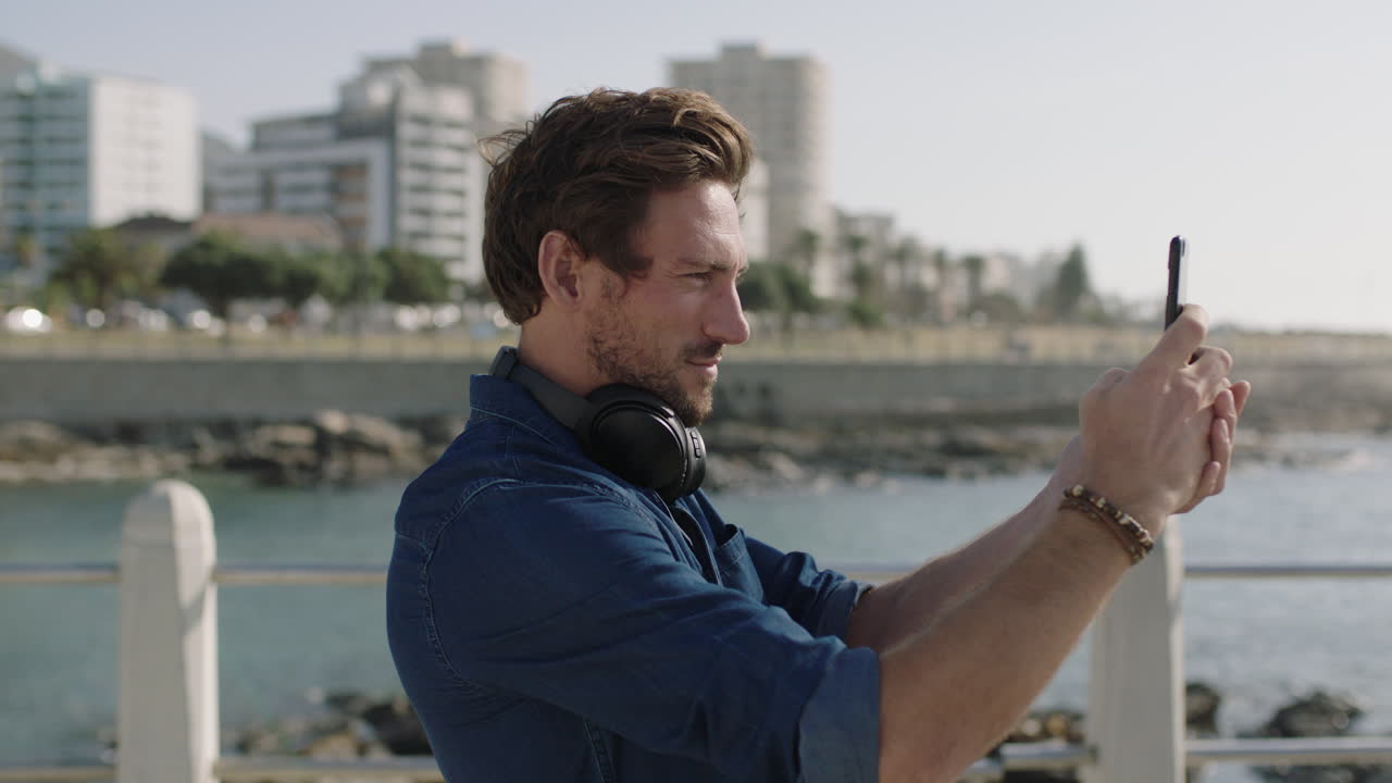 portrait of attractive young man using smartphone taking photo on beautiful seaside beachfront