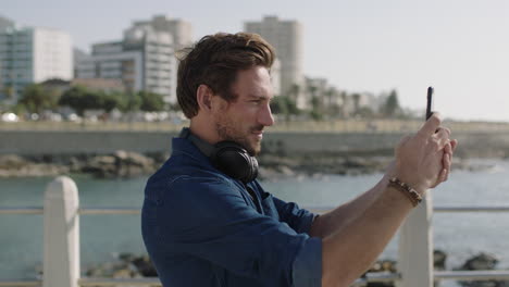 retrato de un joven atractivo usando un teléfono inteligente tomando fotos en la hermosa playa costera