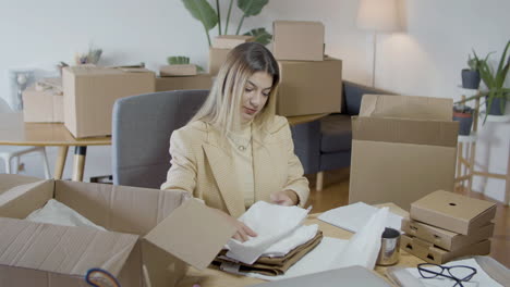 elegant caucasian woman packing purchased clothing and drinking coffee at home office