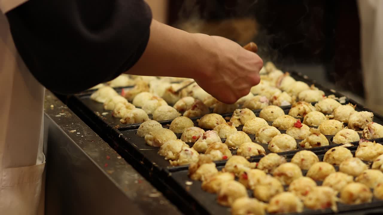 manos girando bolas de takoyaki en una parrilla humeante