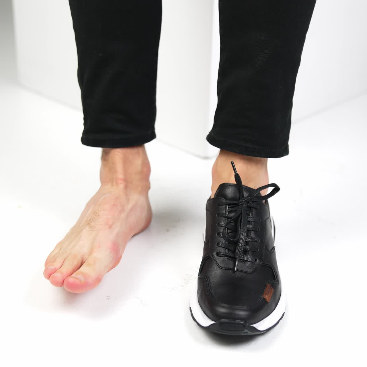 Male legs and feet in a shoe and bare. Man sitting on white chair moves his feet at white backdrop. Close up