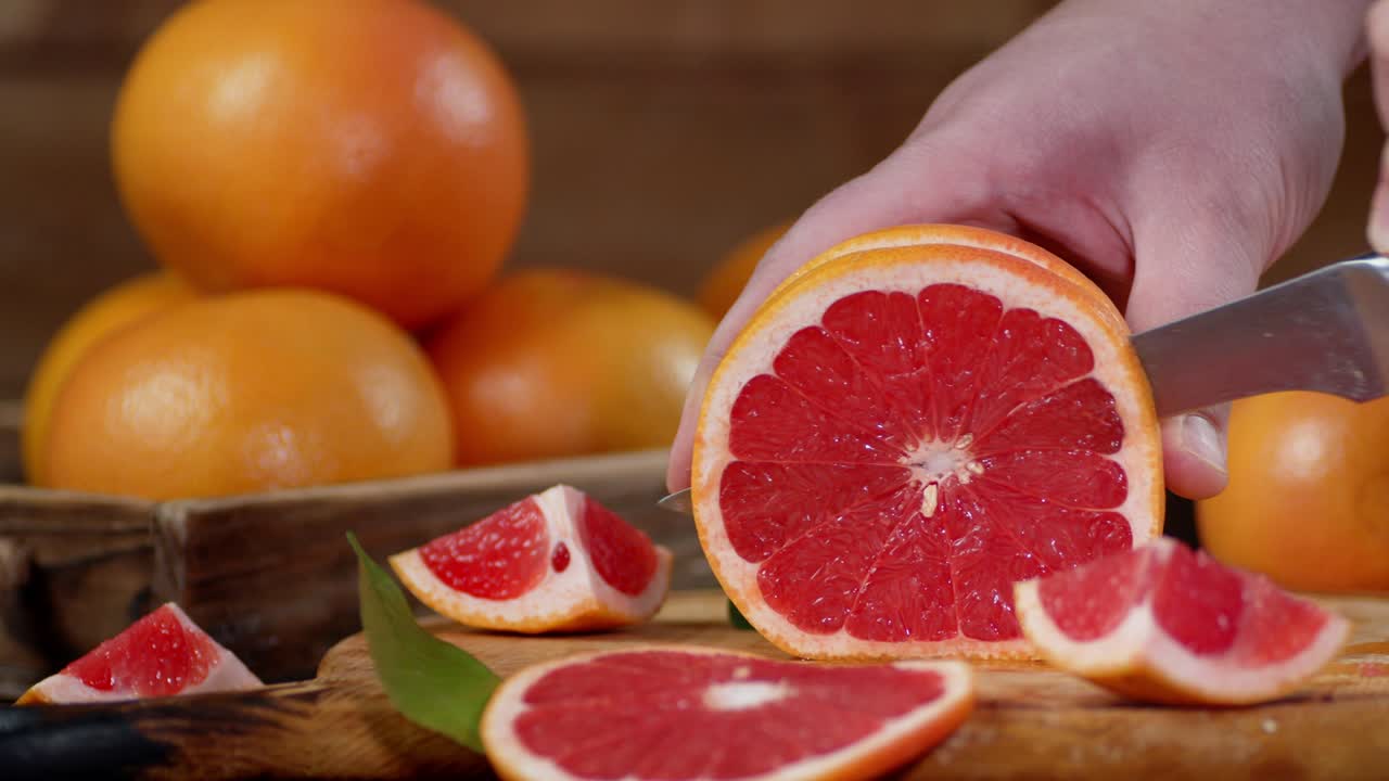 Male hand with a knife cut the grapefruit into slices.